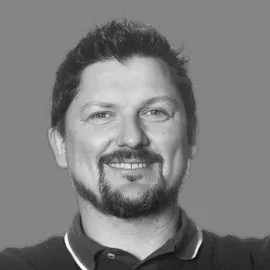 Smiling man with short dark hair and beard against a gray background.