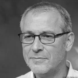 Close-up of a man with glasses, short gray hair, wearing a white shirt.