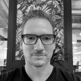 Black and white portrait of a man with glasses in an office setting.